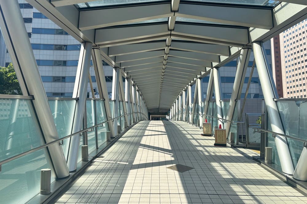 Skywalk at Tennozu Isle Station, sunlight shining through the glass-walled walkway.