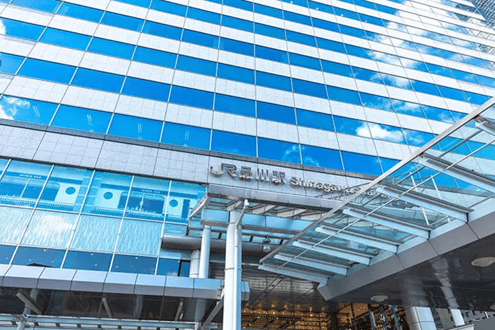 The modern exterior of JR Shinagawa Station building with its name sign against a blue sky.