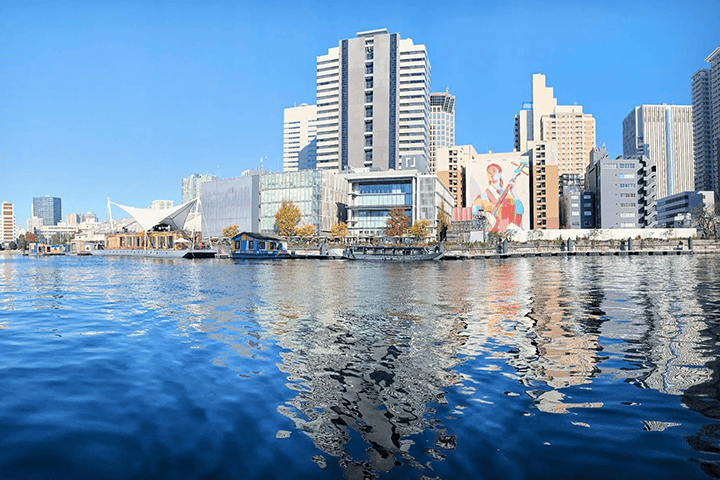 A view of the Tennoz Isle cityscape from the Tennoz Canal, with buildings reflected on the water and an art mural on a wall.