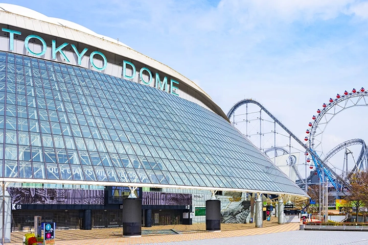 The exterior of the Tokyo Dome, with the amusement park's Ferris wheel and roller coaster located next to it.