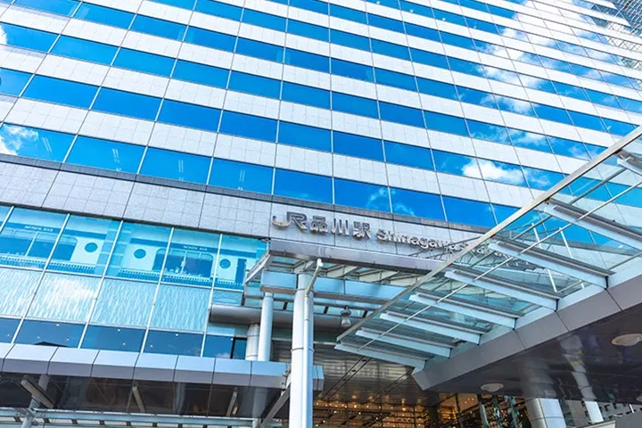 The modern exterior of JR Shinagawa Station building with its name sign against a blue sky.
