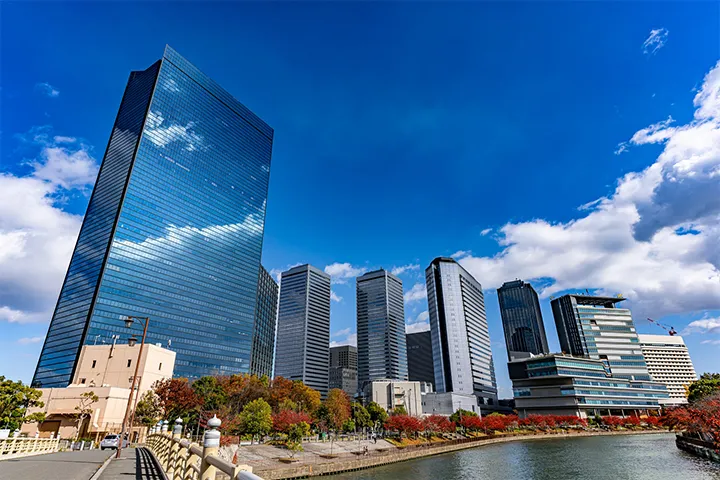The skyline of Osaka Business Park (OBP) skyscrapers along the river, with autumn foliage lining the water's edge.