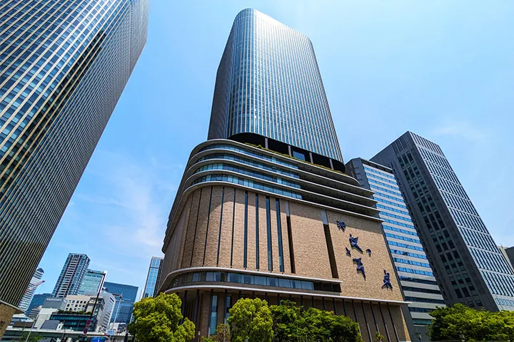 Exterior of Nakanoshima Festival Tower, featuring the brick-colored Festival Hall with its iconic reliefs and the glass-walled skyscraper rising above it.