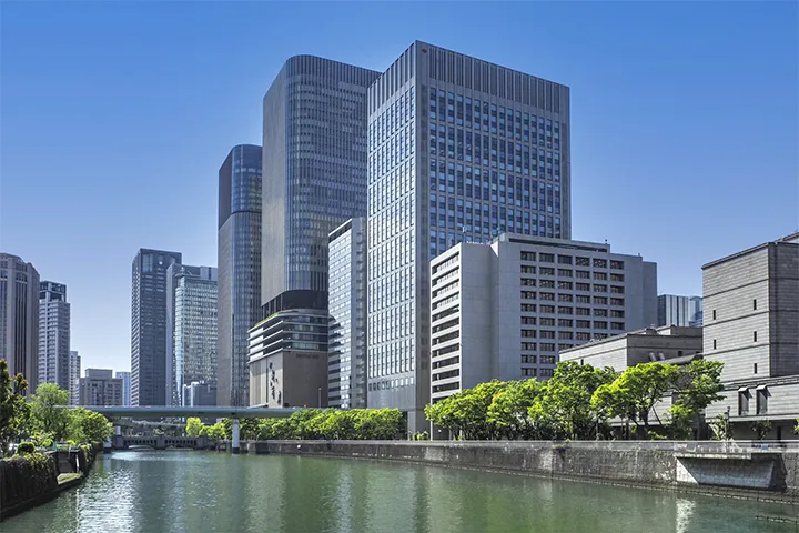 A row of modern skyscrapers in the Yodoyabashi area standing in an orderly fashion. Under a clear blue sky, a sophisticated and urban landscape unfolds.