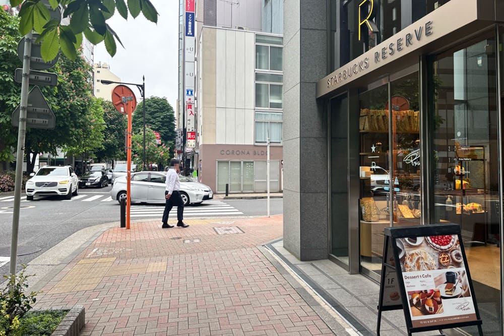 A view of Ginza Marronnier Street, featuring a store entrance with the words “STARBUCKS RESERVE” visible on the right, and a crossroads and crosswalk in the background to the left.