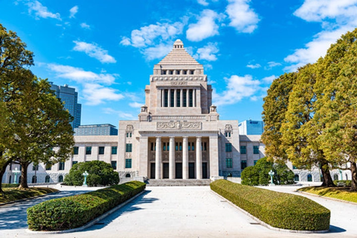 青空の下にそびえ立つ国会議事堂。左右対称の美しい建物と、手前の手入れされた庭。