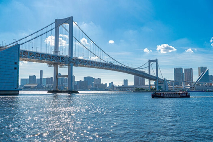 晴天の東京湾に架かるレインボーブリッジ。手前には観光船が浮かんでいる。