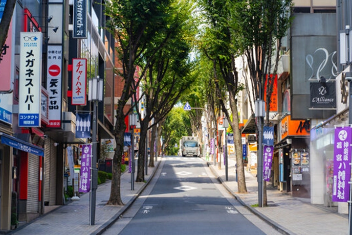 神楽坂の坂道。街路樹が並び、両脇には様々な店舗の看板が並んでいる。