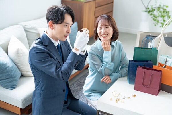 古物商が手袋をして商品を鑑定し、女性が笑顔で見ている。