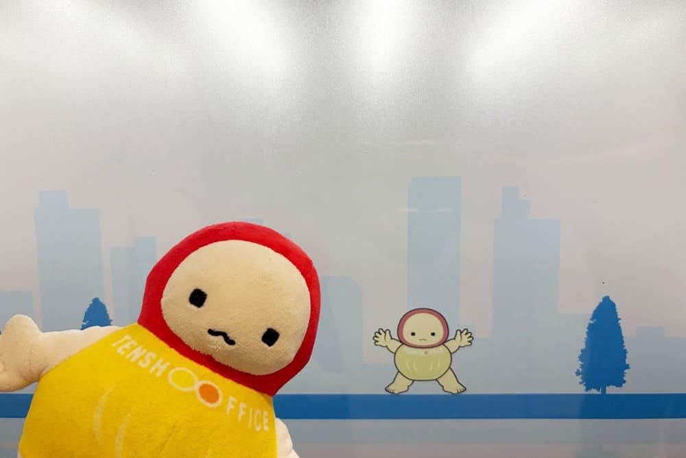 天翔オフィス天王洲ファーストタワー7階エントランスの扉に描かれているてんしょうくん。扉に描かれている自身を見て喜んでいる、てんしょうくんぬいの様子。