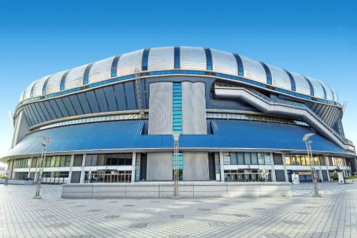 青空の下に立つ、波打つような銀色の屋根と青い外壁が特徴的な京セラドーム大阪の外観。