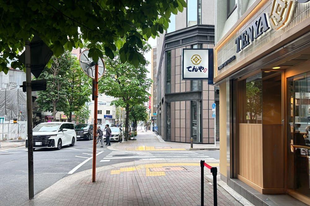右側にてんやの看板と店舗の外観があり、正面に横断歩道や街路樹が見える銀座の通り沿いの風景。