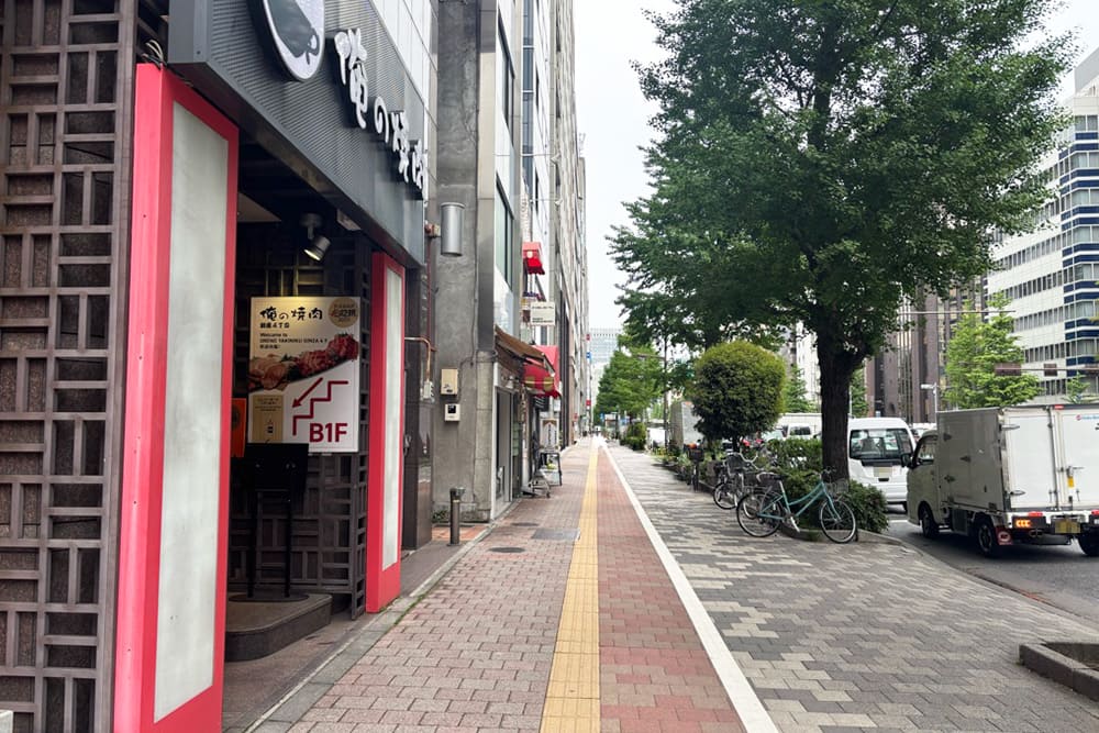 俺の焼肉 銀座4丁目店の入り口と、街路樹のある歩道の風景。
